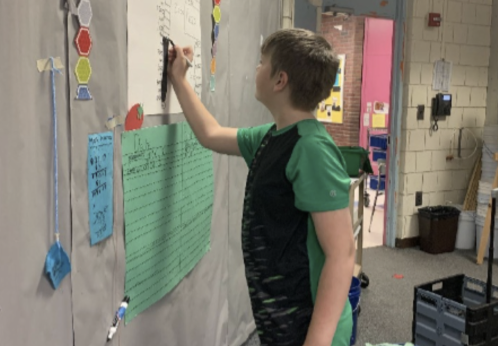 A student writing on a piece of paper on the wall